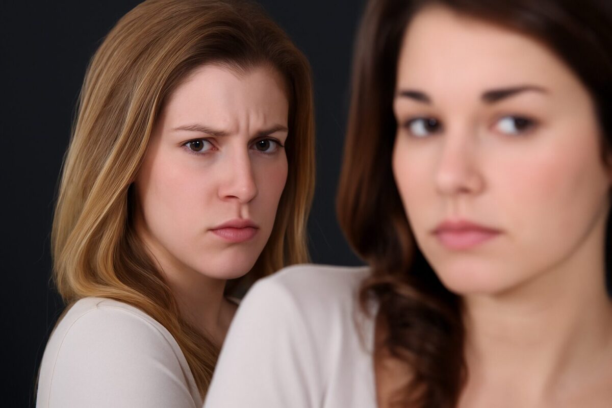 Две молодые женщины, одна из которых смотрит с подозрением и недоверием на другую, находящуюся в размытом фокусе на переднем плане.